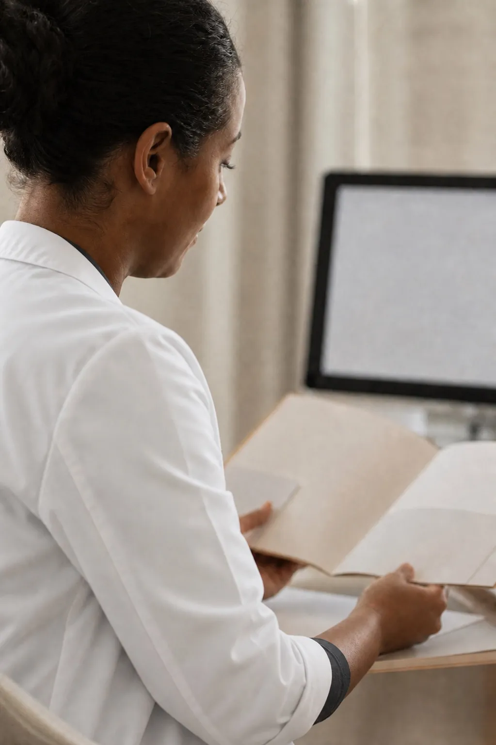 A clinician reviewing a paper record beside a computer